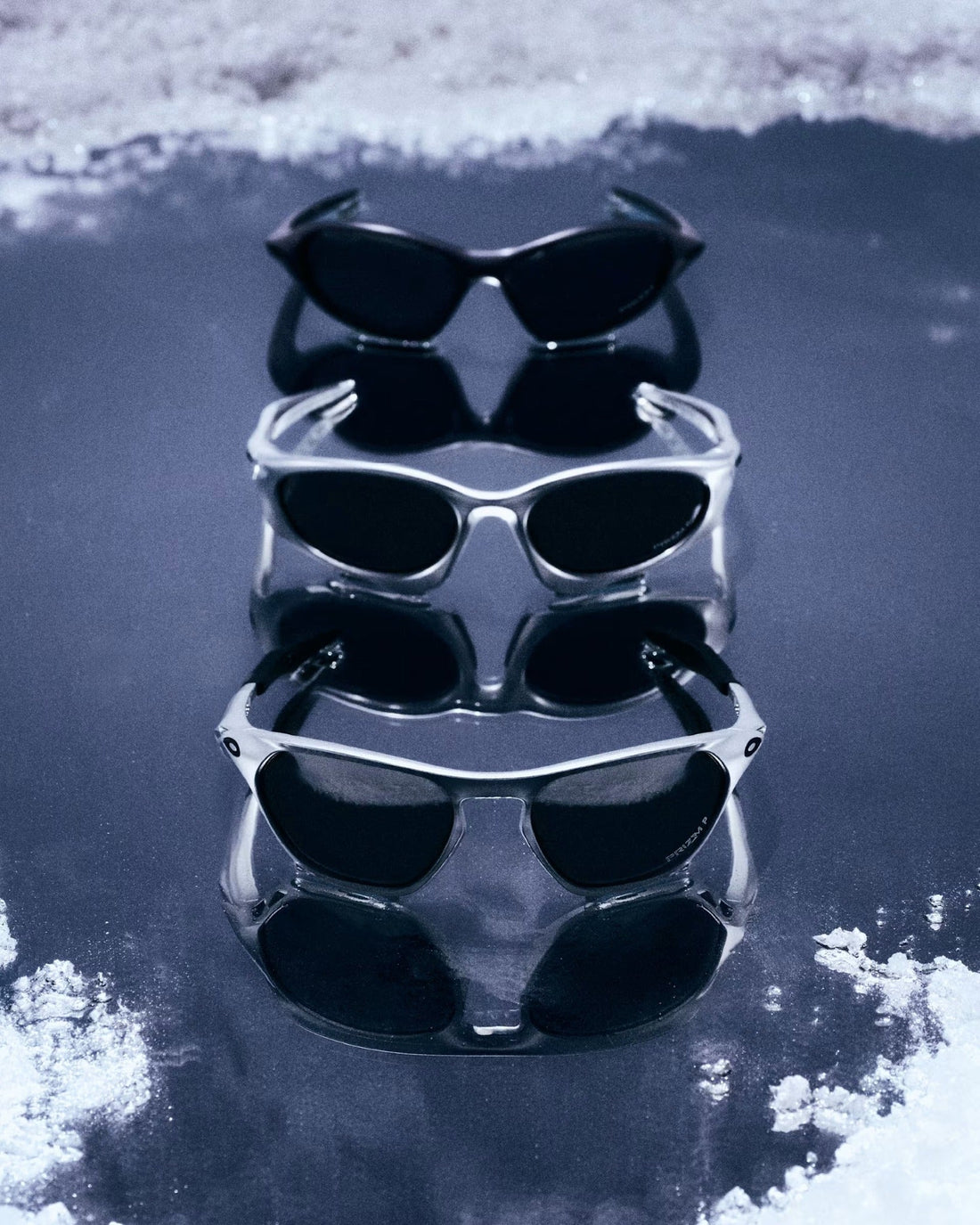 Oakley Jackets Family แว่นกันแดดกรอบดำและเงินสามทรงบนพื้นสะท้อนในแคมเปญ FW26