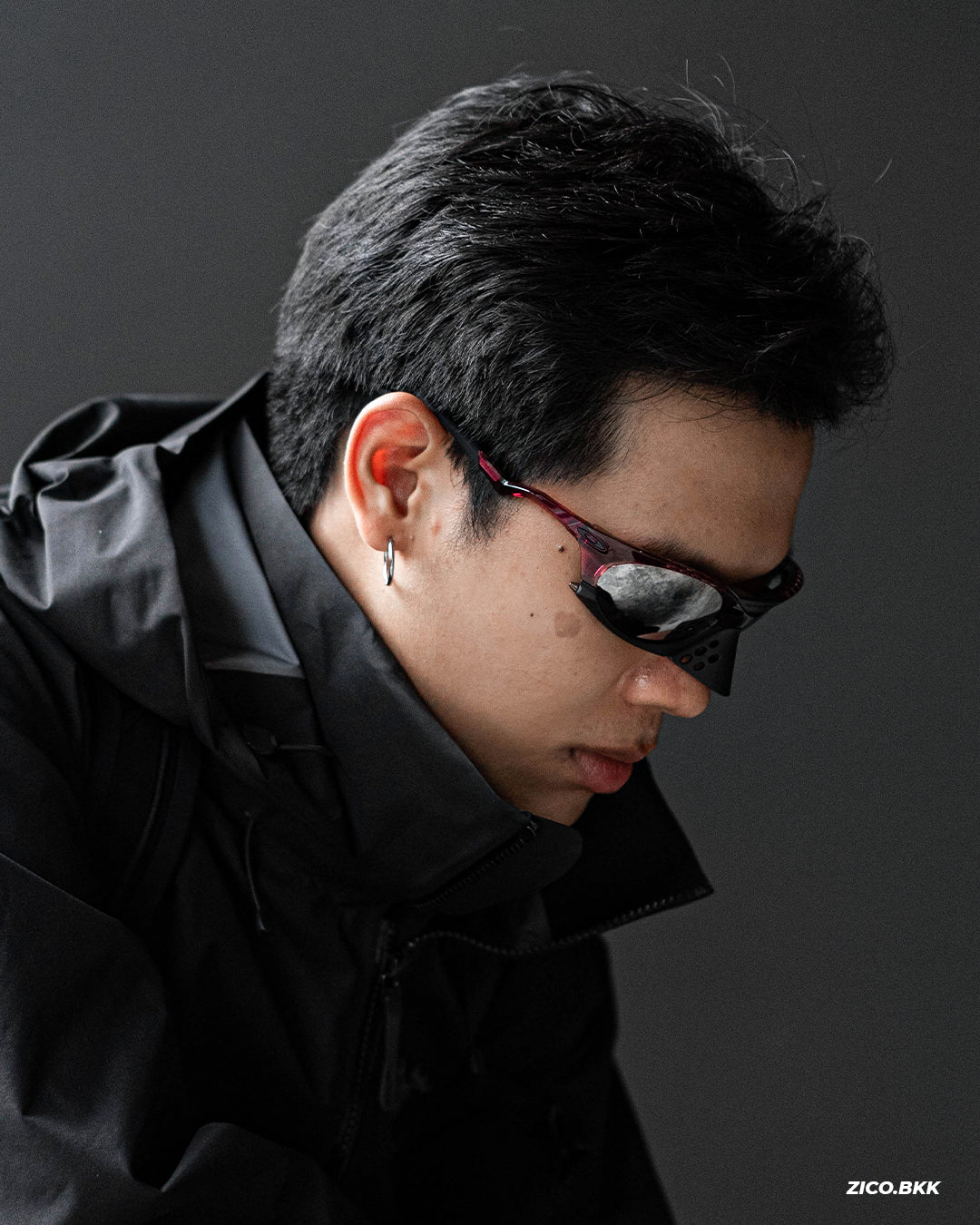 Oakley Plantaris Transparent Iron Red แว่นกันแดดกรอบแดงโปร่งพร้อม Noseguard มุมใกล้ขณะสวมกับเสื้อคลุมสีดำ